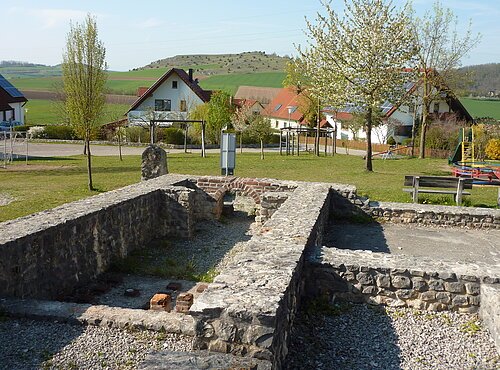 Ein Blick auf die Mauern des ehemaligen Römerbads in Großsorheim. Im Hintergrund sind ein Spielplatz und Wohnhäuser zu sehen.