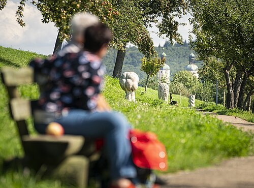 Zwei Wanderer auf einer Bank am Andachtsweg zur Wallfahrtsbasilika Maria Brünnlein.