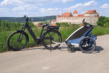 E-Bike mit Fahrradanhänger für Kinder auf einem Radweg bei Harburg. Im Hintergrund ist das Schloss Harburg zu sehen.