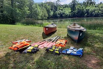 Zwei Kanus an einer Anlegestelle an der Wörnitz. Davor befinden sich Schwimmwesten und Paddel.