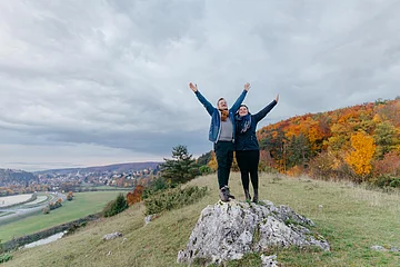 Ein Pärchen unterwegs auf der Heide bei Harburg vor einem herbstlich buntem Wald. Links im Hintergrund sieht man die Wörnitz und die Stadt Harburg.