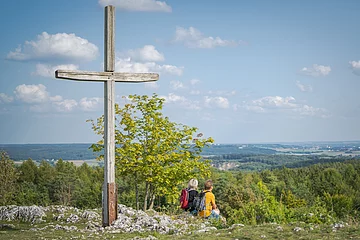 Zwei Wanderer sitzen neben dem Gipfelkreuz auf dem Bockberg und genießen die Aussicht