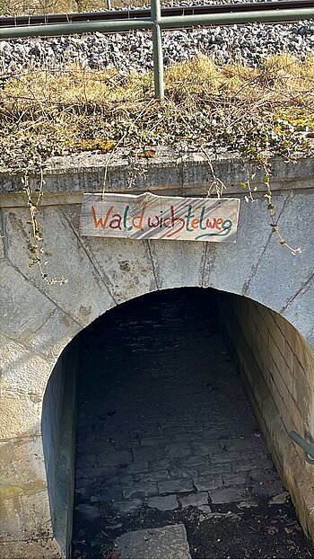Der Wichtelwegeingang an einer Bahnbrücke mit einem Schild was den Weg weißt