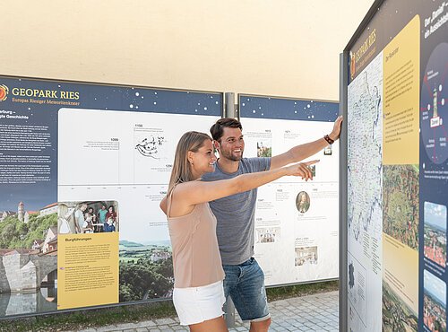 Ein Mann und eine Frau betrachten eine Informationstafel über den Geopark Ries.