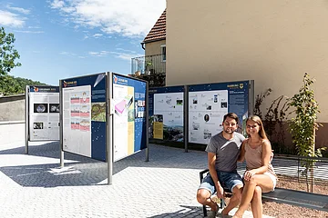 Ein Mann und eine Frau sitzen auf einer Bank bei mehreren Informationstafeln über den Geopark Ries.