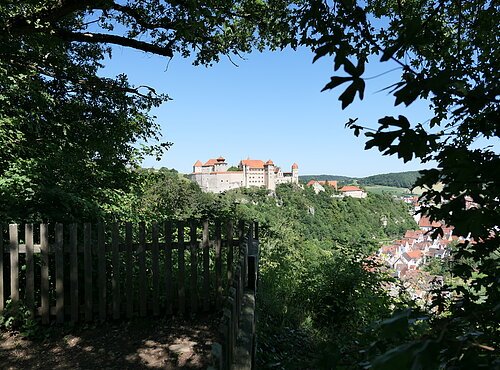Unter dem Blätterdach eines Aussichtspunktes heraus geht der Blick zur Burg Harburg auf einem bewaldeten Hügel.