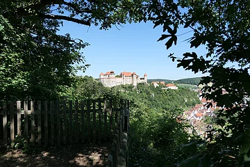Unter dem Blätterdach eines Aussichtspunktes heraus geht der Blick zur Burg Harburg auf einem bewaldeten Hügel.