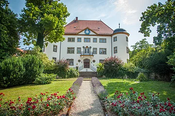 Blick auf das Schloss Reimlingen mit dem davor liegenden Park mit seinen Blumenbeeten und Bäumen.
