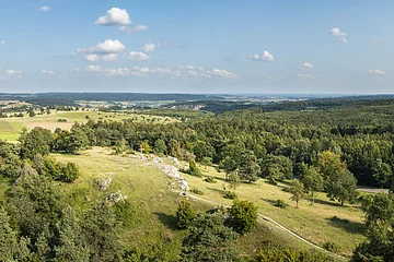Drohnenfoto vom Bockberg bei Harburg mit grünen Hügeln und blauem Himmel. In der Mitte das Gipfelkreuz des Bockbergs
