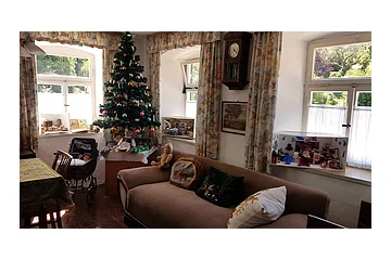 Wohnzimmer mit Weihnachtsbaum, Sofa, Puppen, Puppenwagen und Fenstern mit Gardinen und Blick ins Grüne