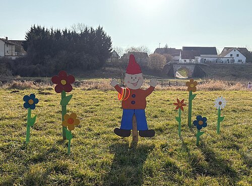 Ein Wichtel aus Holz mit bunten Blumen darum