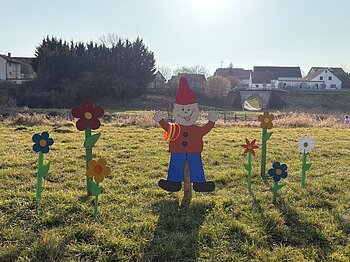 Ein Wichtel aus Holz mit bunten Blumen darum