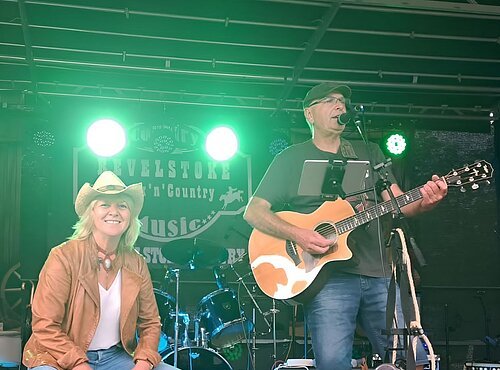 Dargestellt sind die Künstler Tom und Bine. Tom spielt Gitarre und singt, während Bine auf einer Kistentrommel spielt