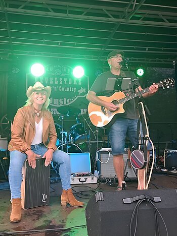 Dargestellt sind die Künstler Tom und Bine. Tom spielt Gitarre und singt, während Bine auf einer Kistentrommel spielt