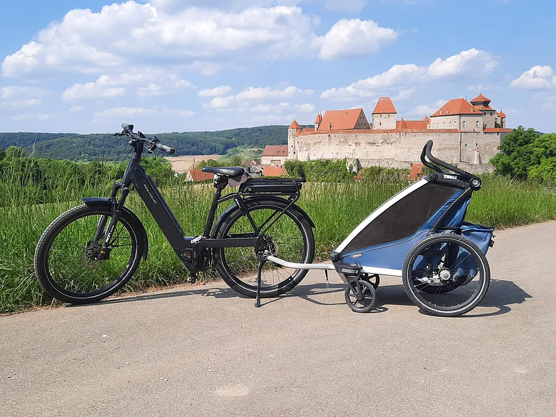 E-Bike mit Fahrradanhänger für Kinder in Harburg E-Bike mit Fahrradanhänger für Kinder auf einem Radweg bei Harburg. Im Hintergrund ist das Schloss Harburg zu sehen.