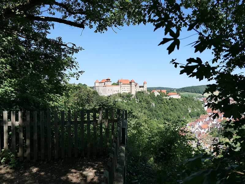 Unter dem Blätterdach eines Aussichtspunktes heraus geht der Blick zur Burg Harburg auf einem bewaldeten Hügel.